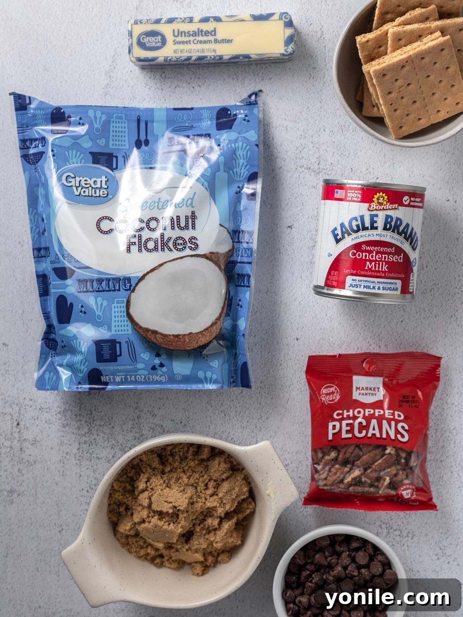 Top down view of the seven simple ingredients for Magic Bars: butter, brown sugar, graham crackers, sweetened condensed milk, chocolate chips, pecans, and shredded coconut arranged neatly.