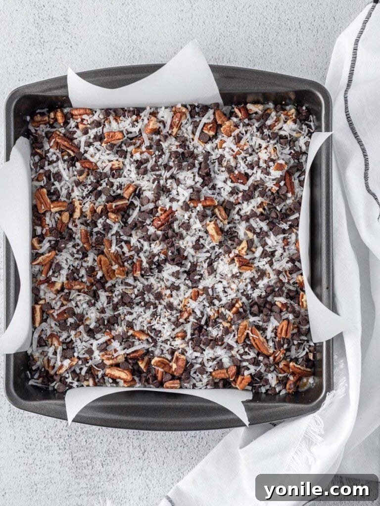 The layered bar mixture neatly arranged in a square baking pan, showing the graham cracker crust topped with sweetened condensed milk and various toppings.