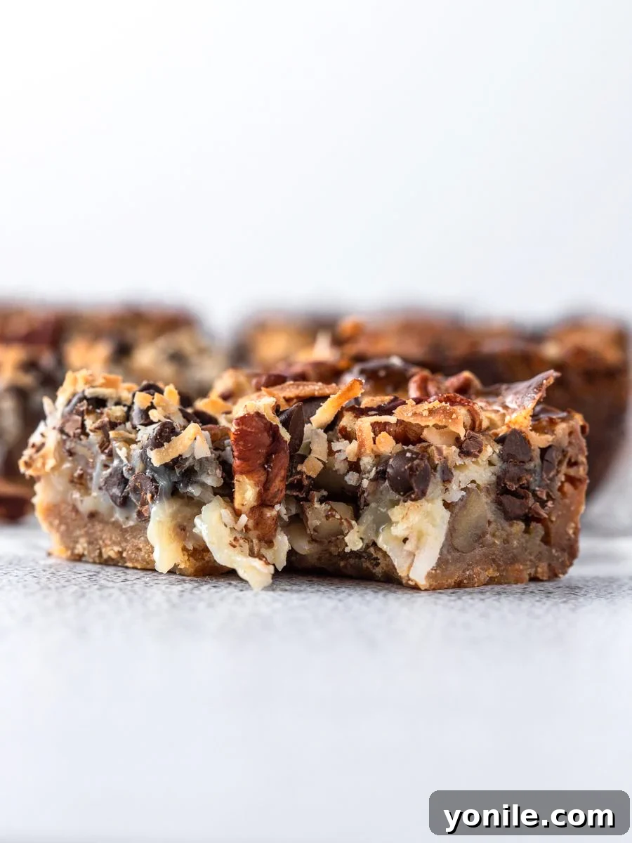 Side view shot of a single magic bar, showing the inside after a bite, highlighting the gooey caramel layer, chocolate chips, and coconut flakes.