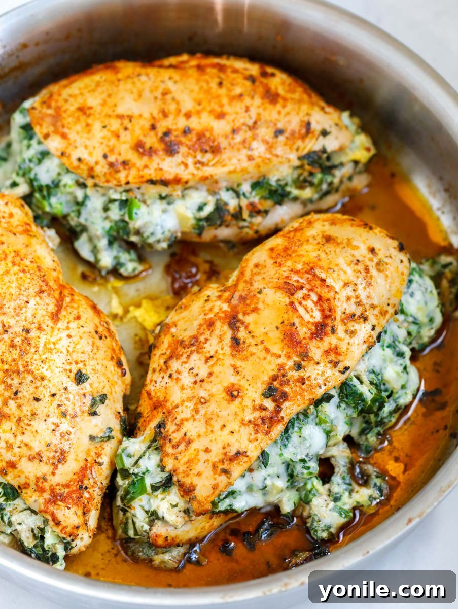 Side shot of three perfectly cooked spinach stuffed chicken breasts in an oven-safe pan, garnished with herbs.