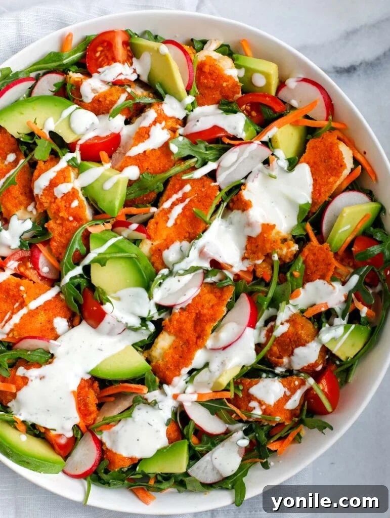 Overhead shot of a generously sized Crispy Buffalo Chicken Salad in a white bowl, showcasing vibrant vegetables and golden-brown chicken pieces.
