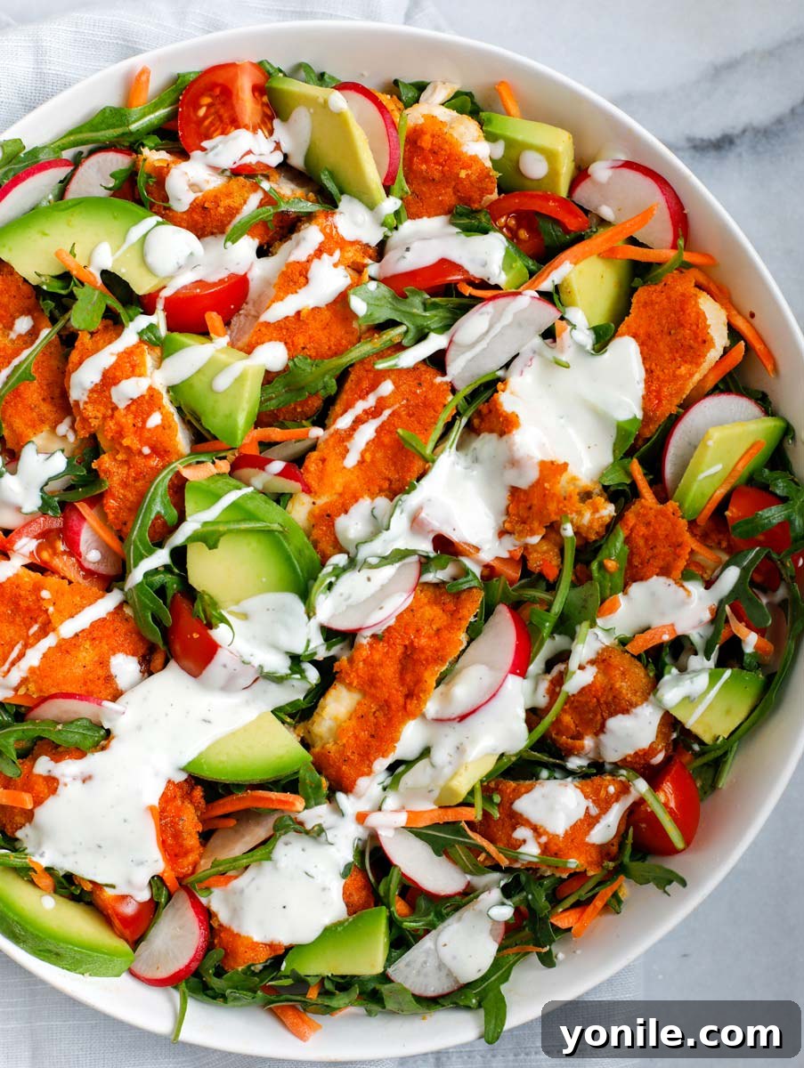A vibrant Crispy Buffalo Chicken Salad complete with creamy ranch dressing drizzled over the top, presented in a clean white bowl.