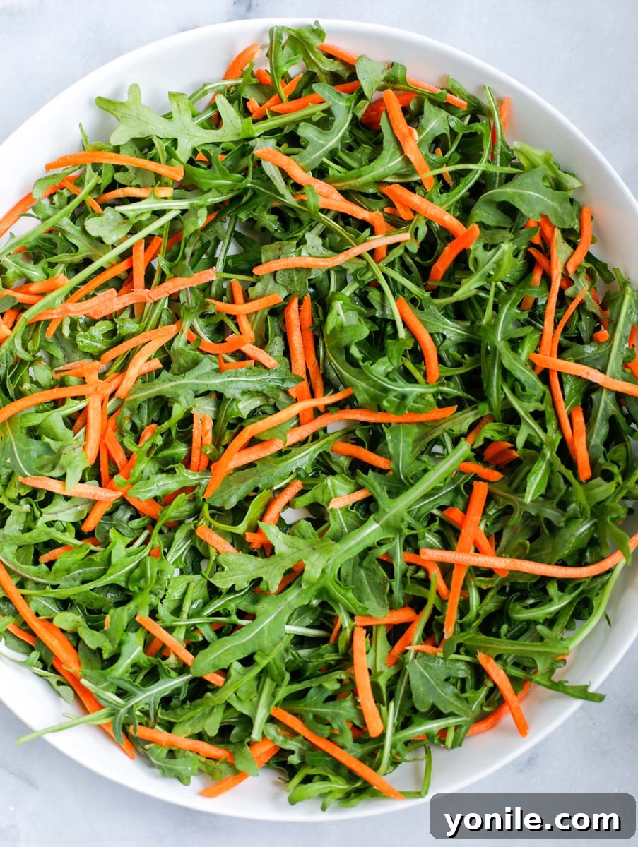 Baby arugula and shredded carrots combined in a bowl, showing a vibrant color contrast.