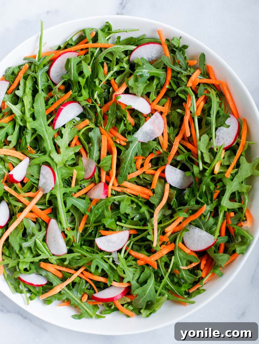 A mix of arugula, radishes, and shredded carrots elegantly presented in a white bowl, forming the base of the salad.