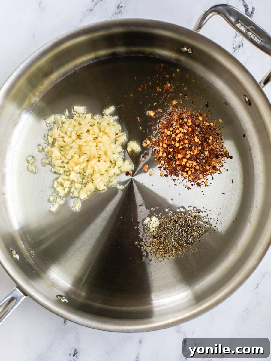 Top-down shot of garlic, pepper, and chili flakes sizzling in olive oil in a skillet.