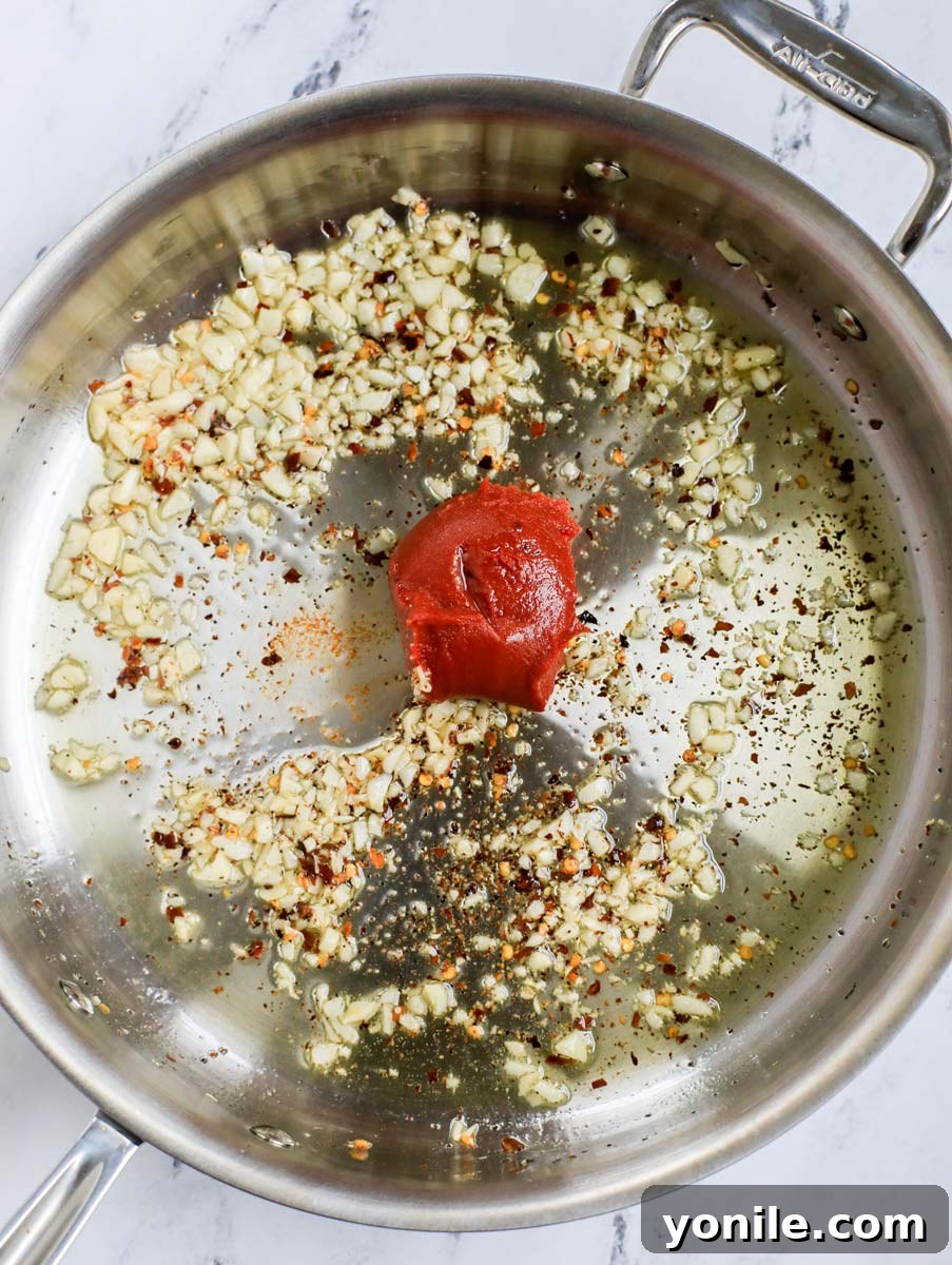 Top-down shot of tomato paste added to the skillet with aromatics.