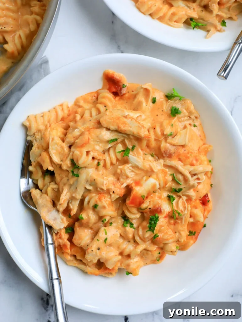 A close-up of a generous serving of golden, bubbly Buffalo Chicken Mac and Cheese on a white plate, garnished with fresh parsley.
