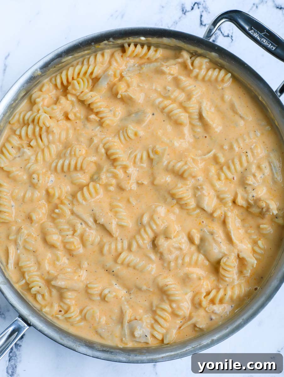Pasta, chicken, and sauce expertly mixed together in a large pot, creating a harmonious blend.