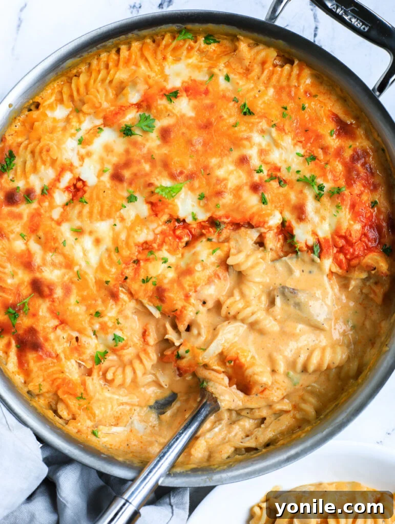 A tantalizing top-down view of the freshly baked Buffalo Chicken Mac and Cheese in a skillet, with a serving spoon nestled in, showing the rich, cheesy interior.