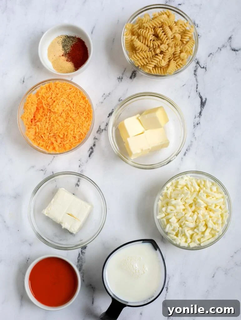 All the ingredients for Buffalo Chicken Mac and Cheese laid out on a wooden board: pasta, shredded chicken, milk, various cheeses, butter, flour, spices, and a bottle of buffalo sauce.