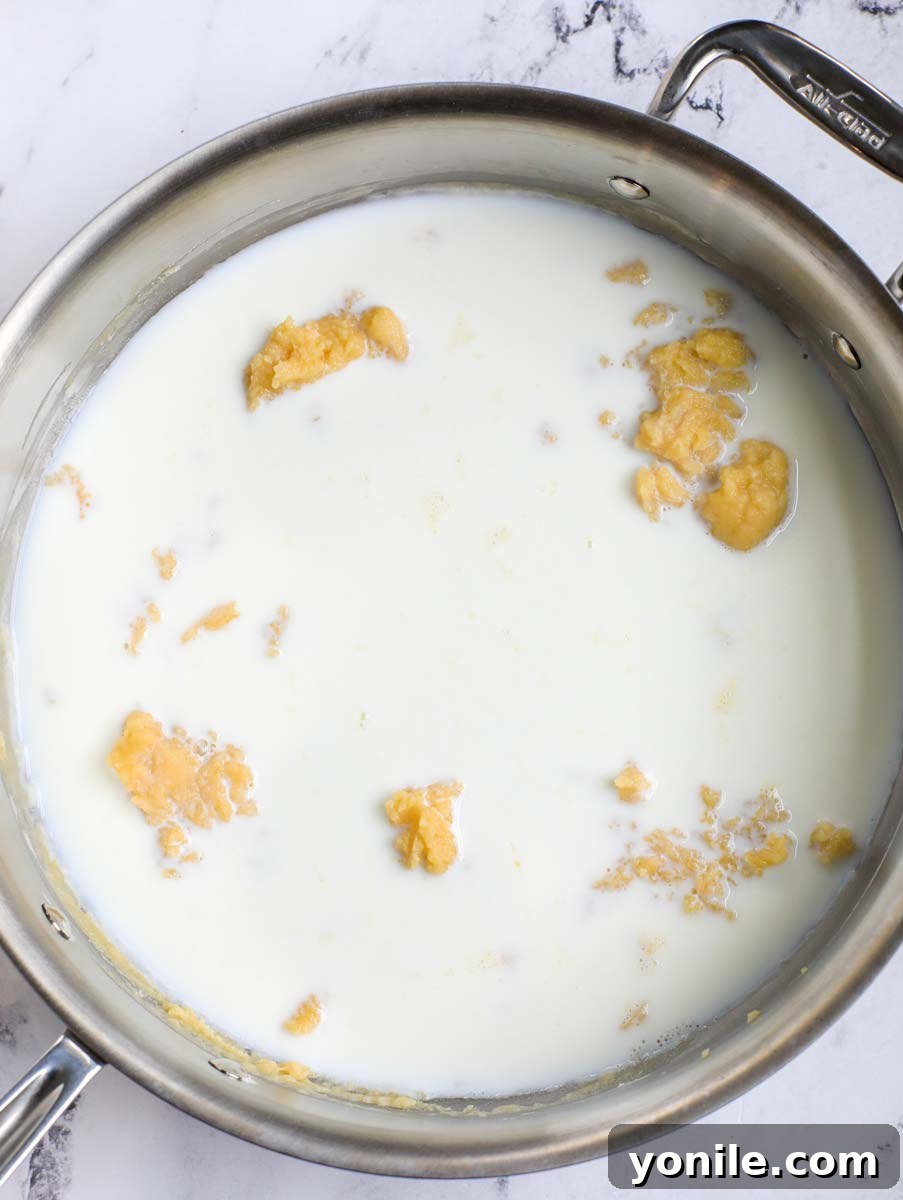 Whole milk being poured into the skillet with the roux, to create the béchamel base.