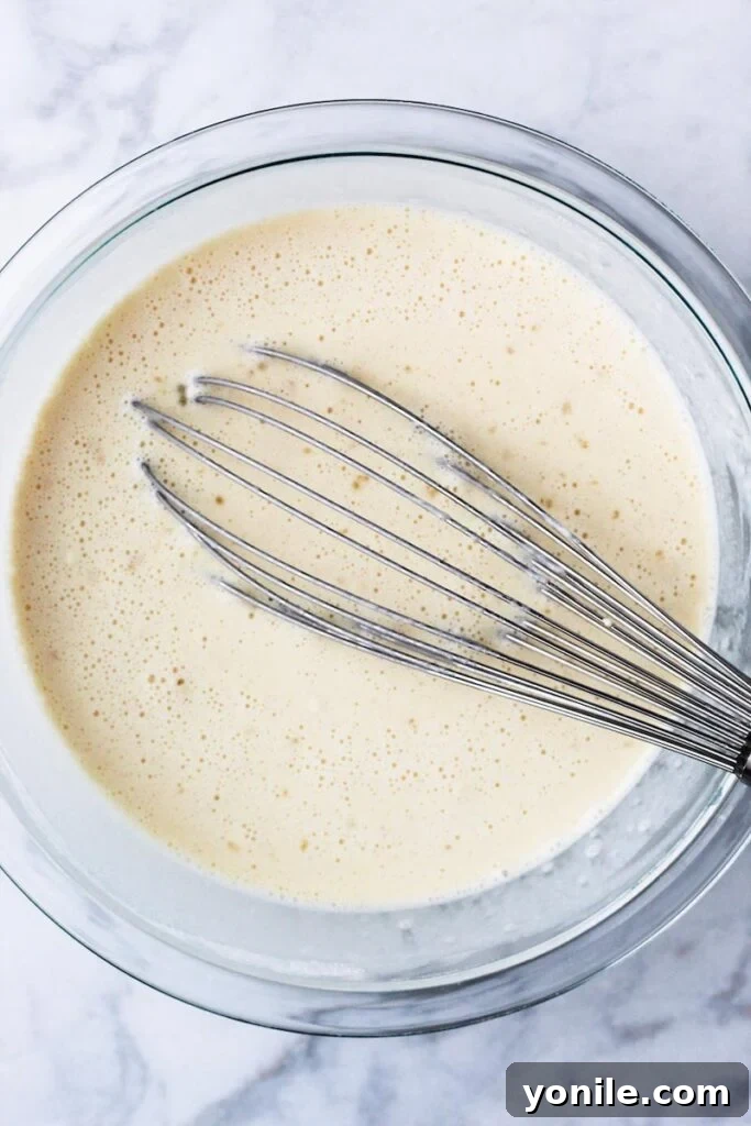 A hand whisking batter in a mixing bowl, illustrating the first step of crepe making.