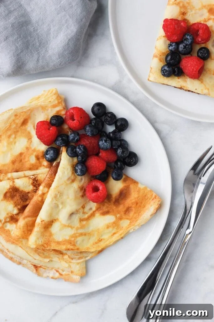 Beautifully presented crepes on a plate, adorned with fresh berries and a dusting of powdered sugar.