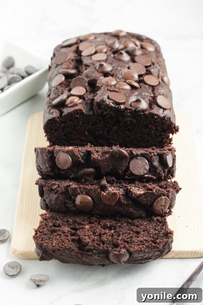 A perfectly sliced loaf of rich chocolate banana bread on a rustic wooden board, showing its moist texture and abundant chocolate chips.