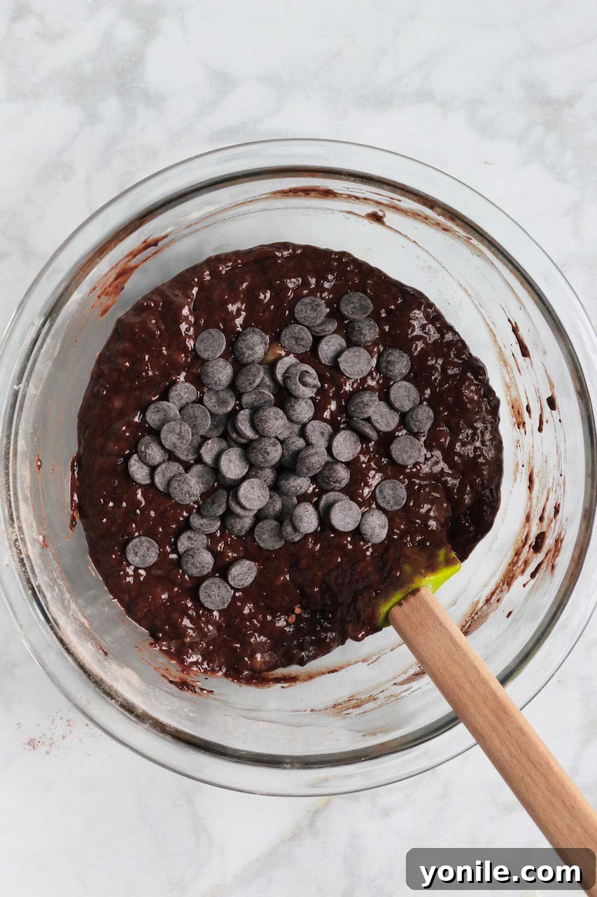 Wet and dry ingredients for chocolate banana bread combined in a bowl, with chocolate chips folded in.