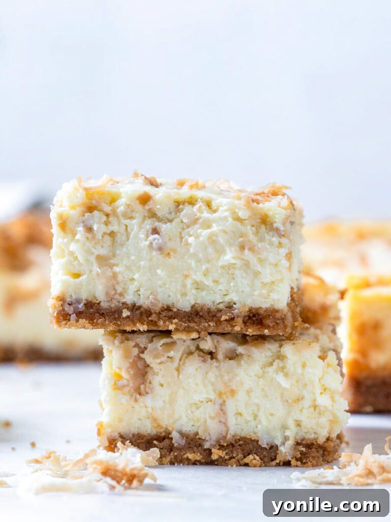 coconut cheesecake bars stacked on top of each other, showcasing their creamy texture and toasted coconut topping