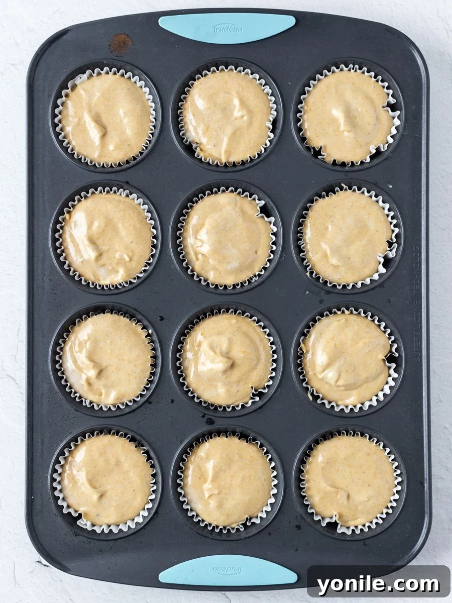 Top down shot of mini pumpkin cheesecakes in a muffin mold, freshly filled and ready for baking, showcasing the smooth filling on the chocolate crust.