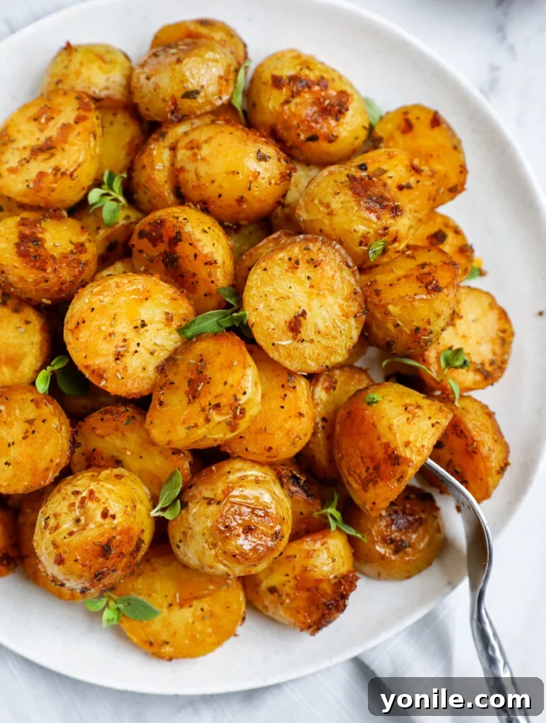 Crispy Oven Roasted Baby Potatoes 2 Top down shot of oven roasted baby potatoes on a white dish, garnished with fresh herbs.