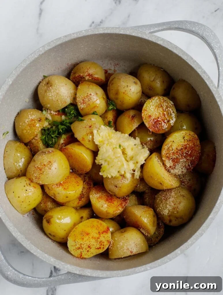 Crispy Oven Roasted Baby Potatoes 4 Top down shot of potatoes being tossed with herbs, garlic, and olive oil in a white bowl.