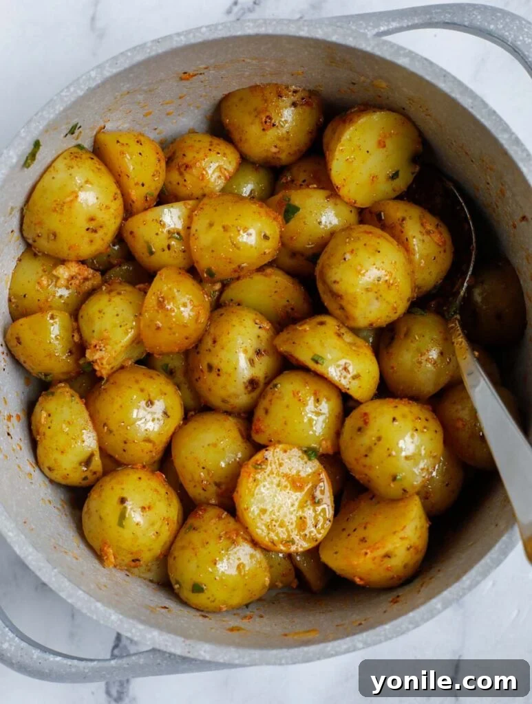 Crispy Oven Roasted Baby Potatoes 5 Potatoes evenly coated in olive oil and seasonings being mixed with a spoon in a white bowl.