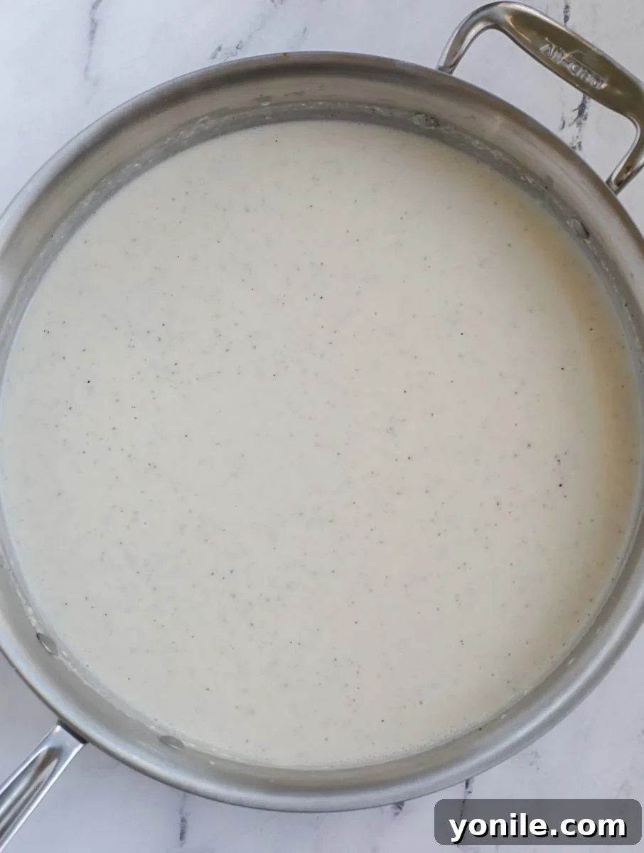 A large silver skillet on a marble counter, filled with a smooth, thick, and creamy casserole sauce, ready for the next ingredients.