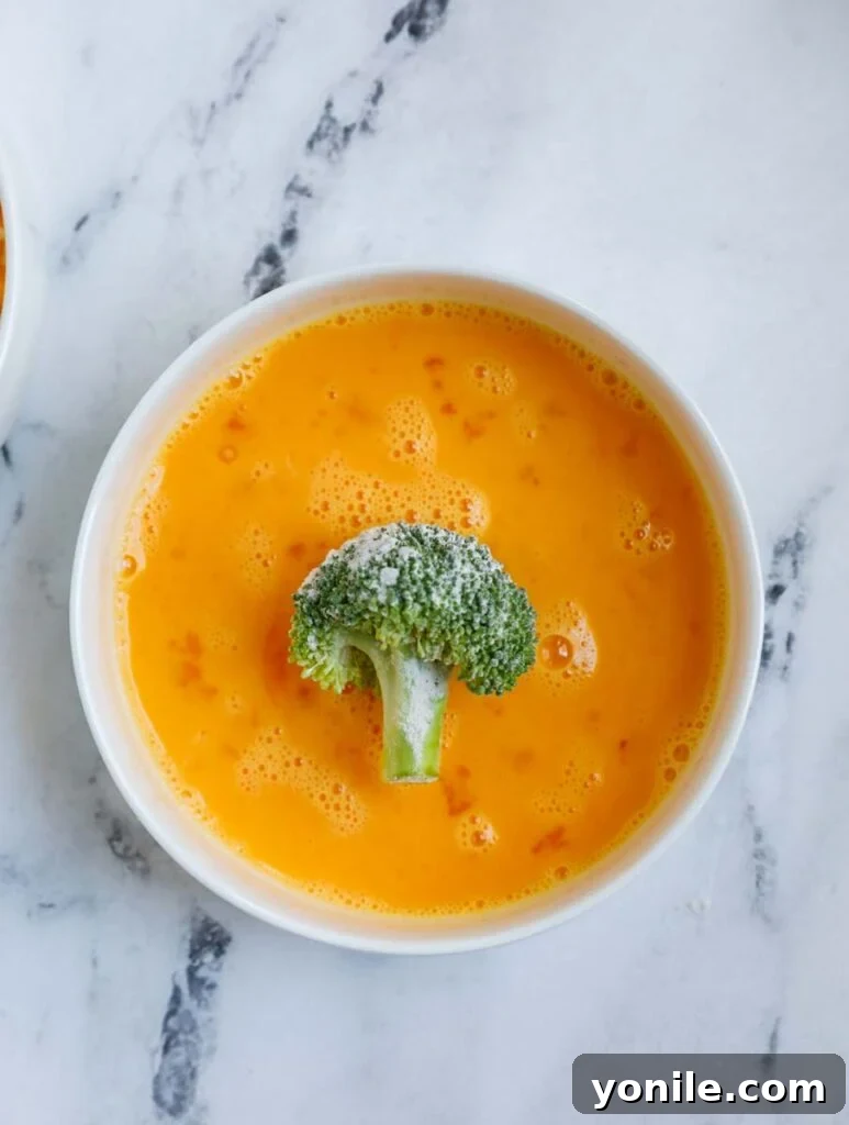 Golden Broccoli Cheese Poppers 5 broccoli in a bowl of egg wash.