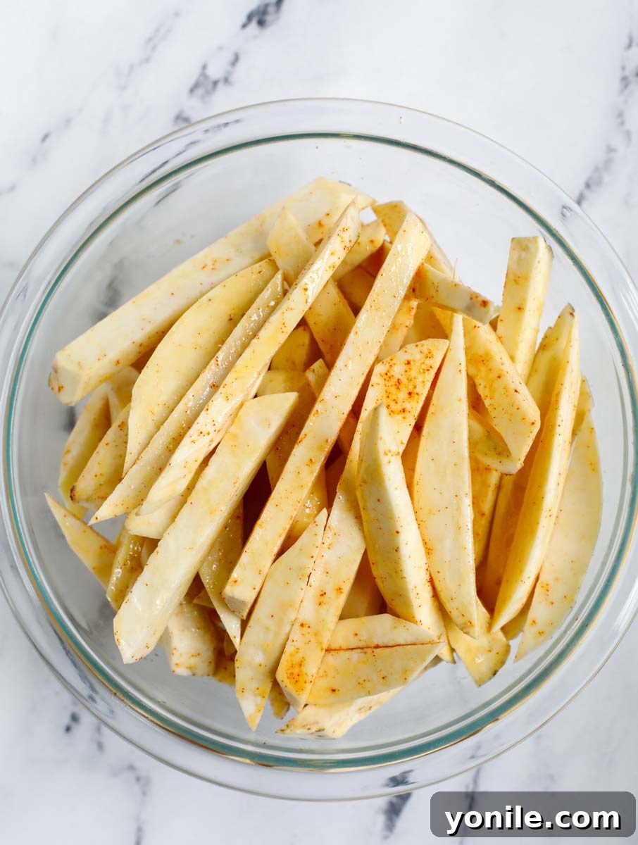 Coating sweet potato slices evenly with oil and seasoning in a bowl.
