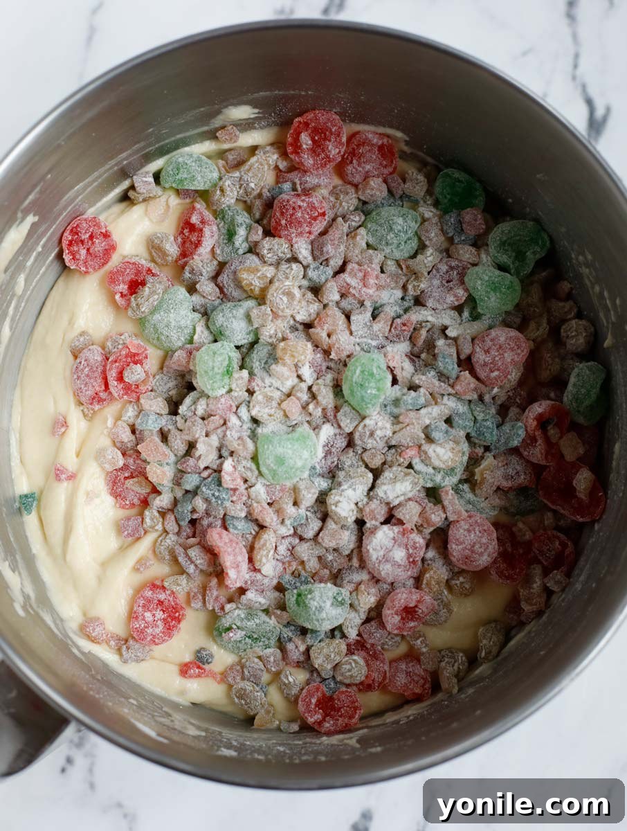 Floured dried fruits being gently folded into the thick cake batter with a spatula.