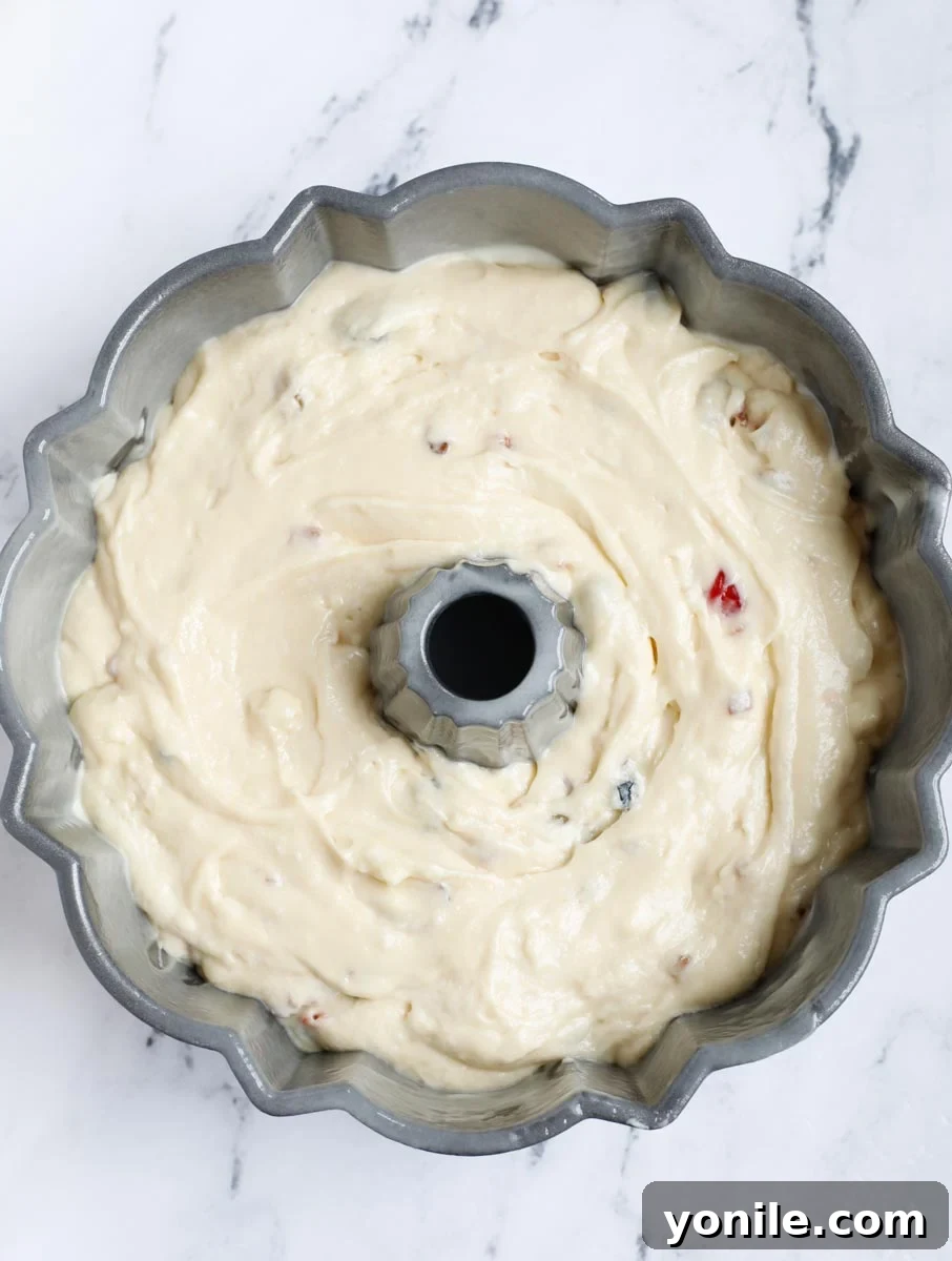 The thick orange fruit cake batter being carefully poured into the prepared Bundt pan.