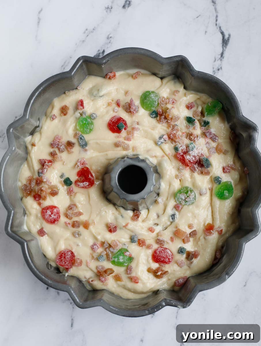 The cake batter in the Bundt pan, beautifully topped with the remaining dried fruits, ready for baking.