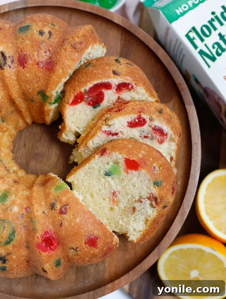 A slice of orange fruit cake served on a rustic wooden plate, showcasing its moist texture and colorful fruit inclusions.