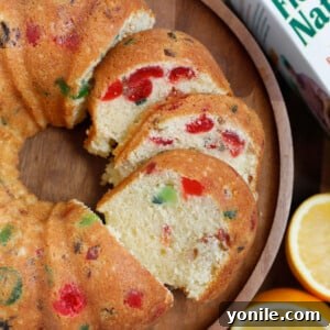 A slice of orange fruit cake served on a rustic wooden plate, showcasing its moist texture and colorful fruit inclusions.