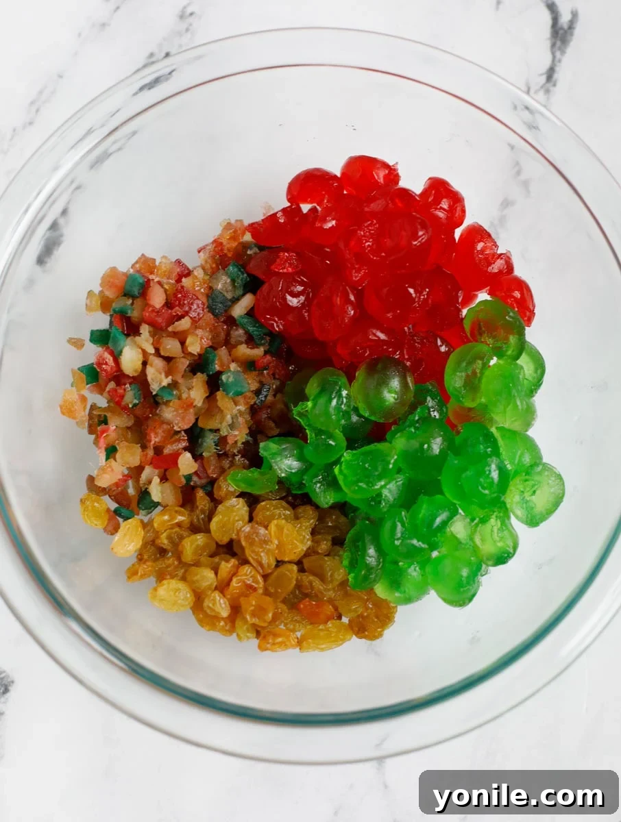 A bowl of various mixed dried fruits, including golden raisins and colorful candied cherries, before being coated.