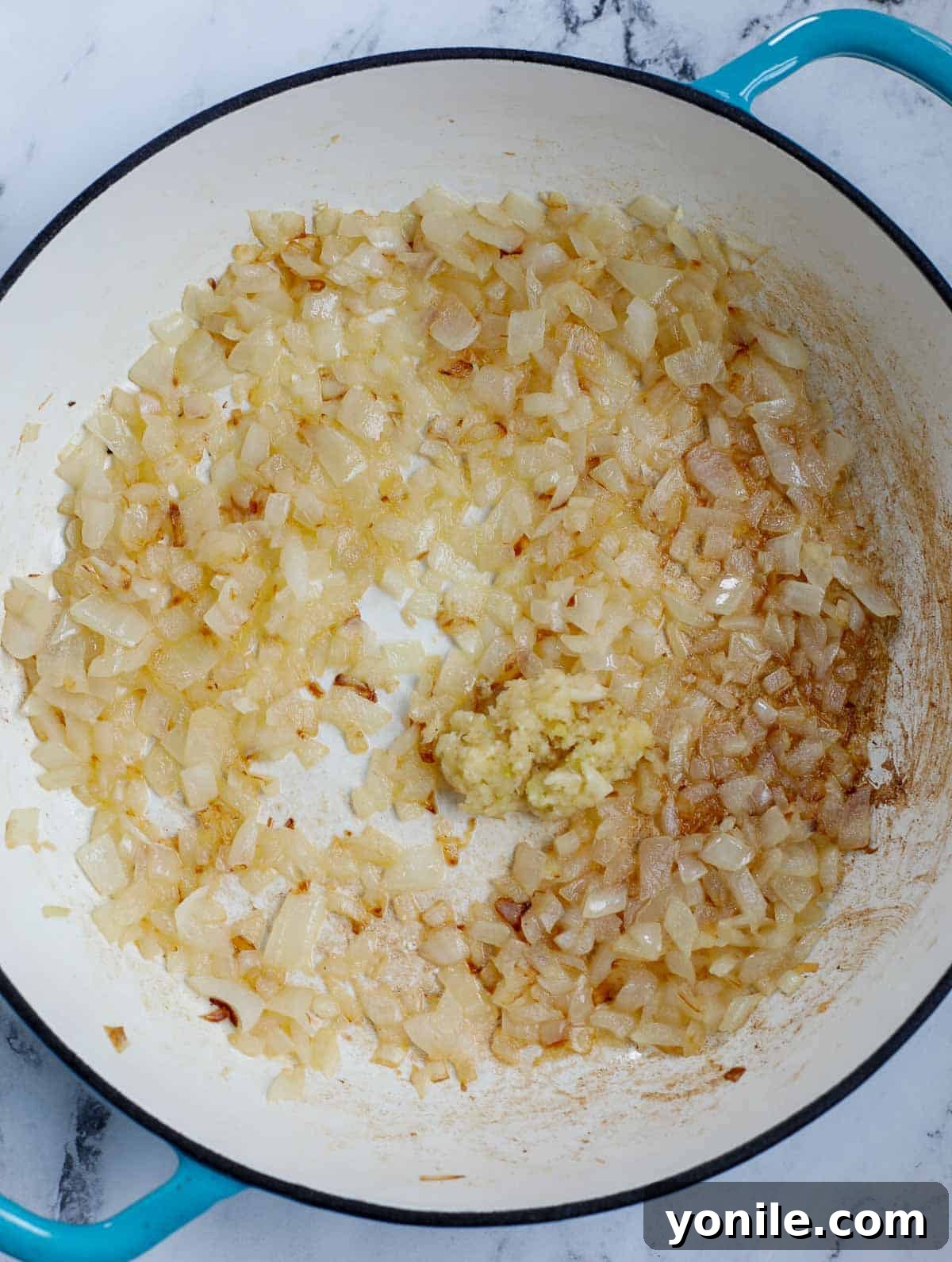 Close-up of sautéed onions and garlic sizzling in a pan, forming the aromatic base for the casserole sauce.