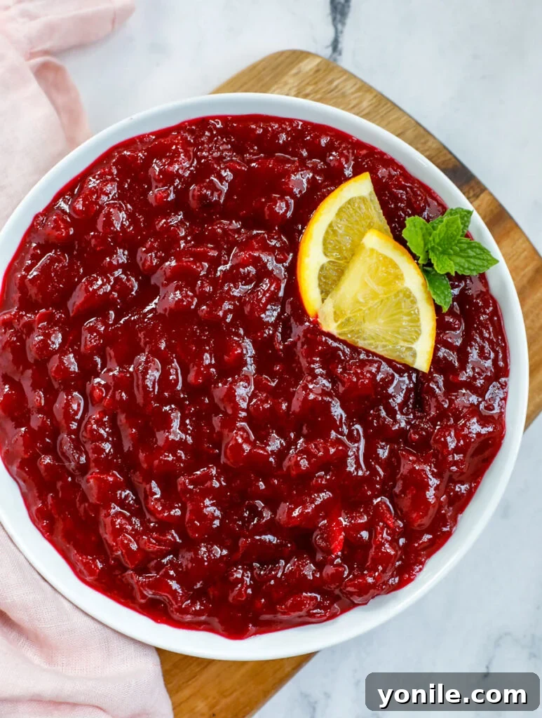 Top-down view of vibrant homemade cranberry sauce served in a white ceramic dish, with a spoon resting in it.