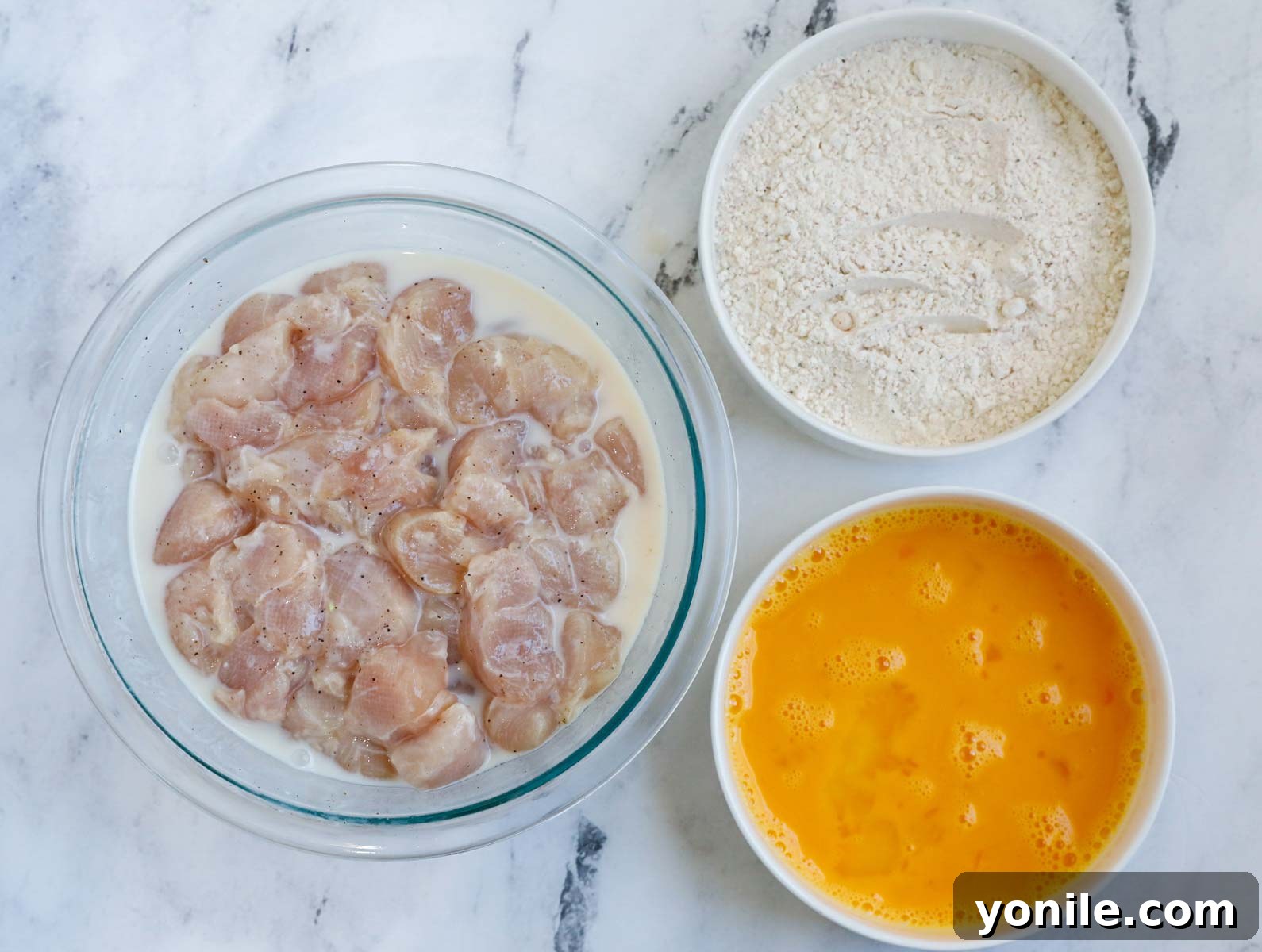 Homemade Chicken Nuggets: Crispy, Juicy, Perfect 3 Top down shot of ingredients for making crispy homemade chicken nuggets, including chicken, buttermilk, flour, and spices.