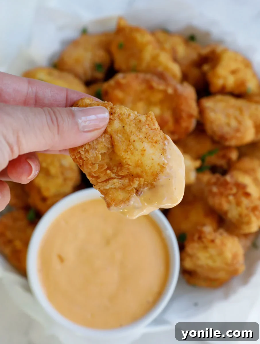 Homemade Chicken Nuggets: Crispy, Juicy, Perfect 7 Female hand holding a piece of homemade chicken nugget dipped in a creamy sauce.