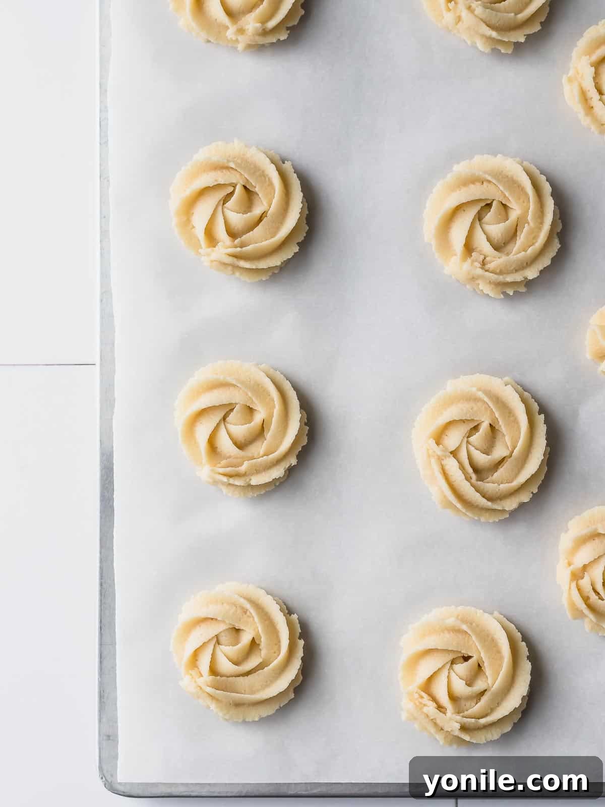 A baking sheet filled with perfectly piped, unbaked Danish butter cookies, featuring various elegant shapes, ready to be chilled and then baked.