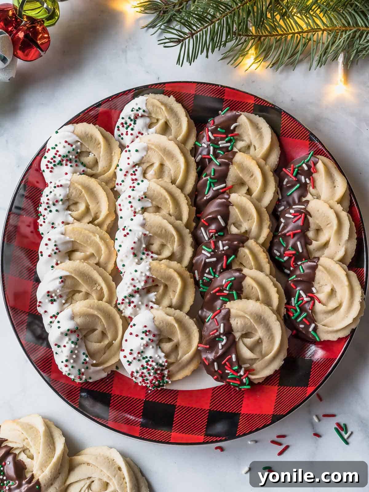 An array of elegantly piped Danish butter cookies, some plain and some dipped in chocolate, beautifully arranged on a festive plaid plate, highlighting their various forms.