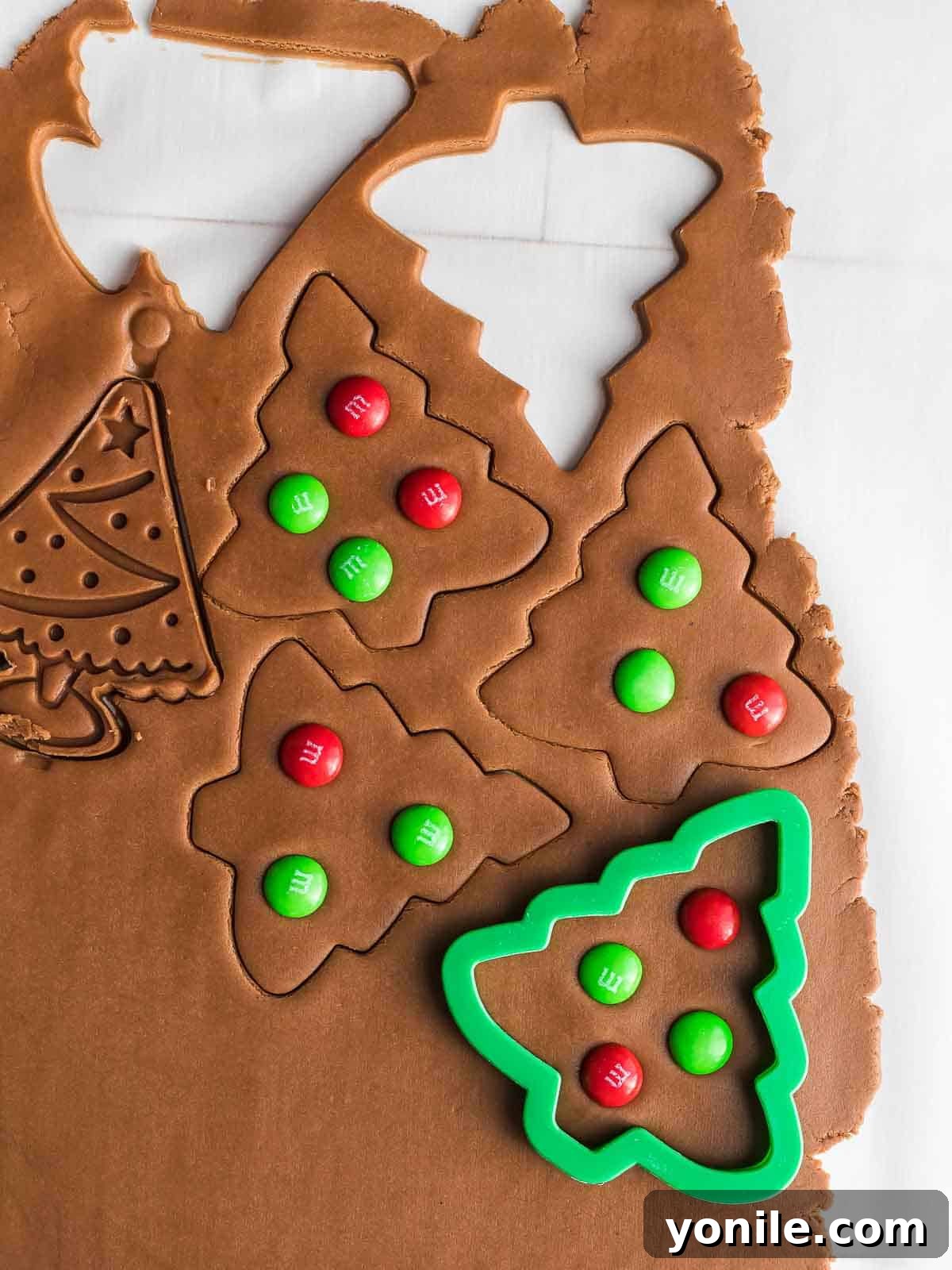 tree cookies being cut with a cookie cutter and decorated with M&M's