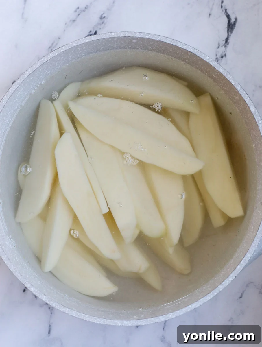 Potatoes in a pot with water, ready to begin the parboiling process, showing whole and sliced potatoes.