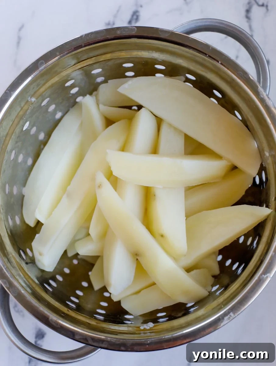 Draining parboiled potato slices in a colander, with steam visibly rising, indicating their readiness for seasoning.