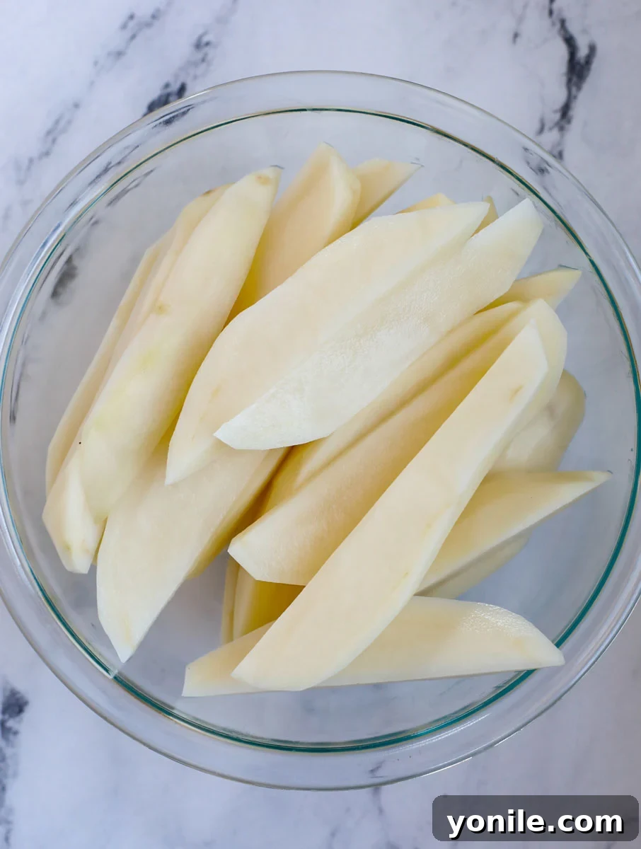 Clean, uniformly cut potato slices in a large mixing bowl, patiently waiting for olive oil and spices.