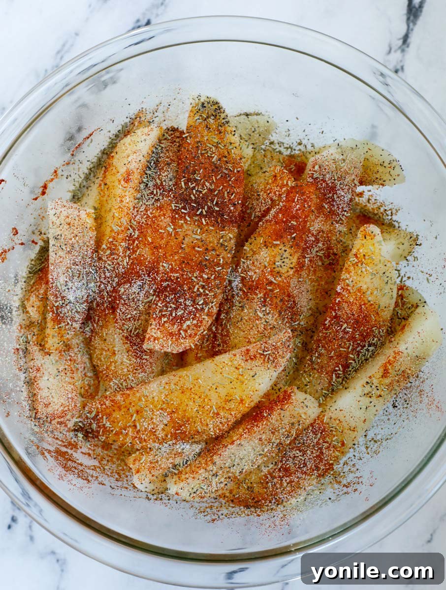 Potato slices in a bowl being gently tossed with olive oil and a vibrant blend of spices, ensuring even coating.