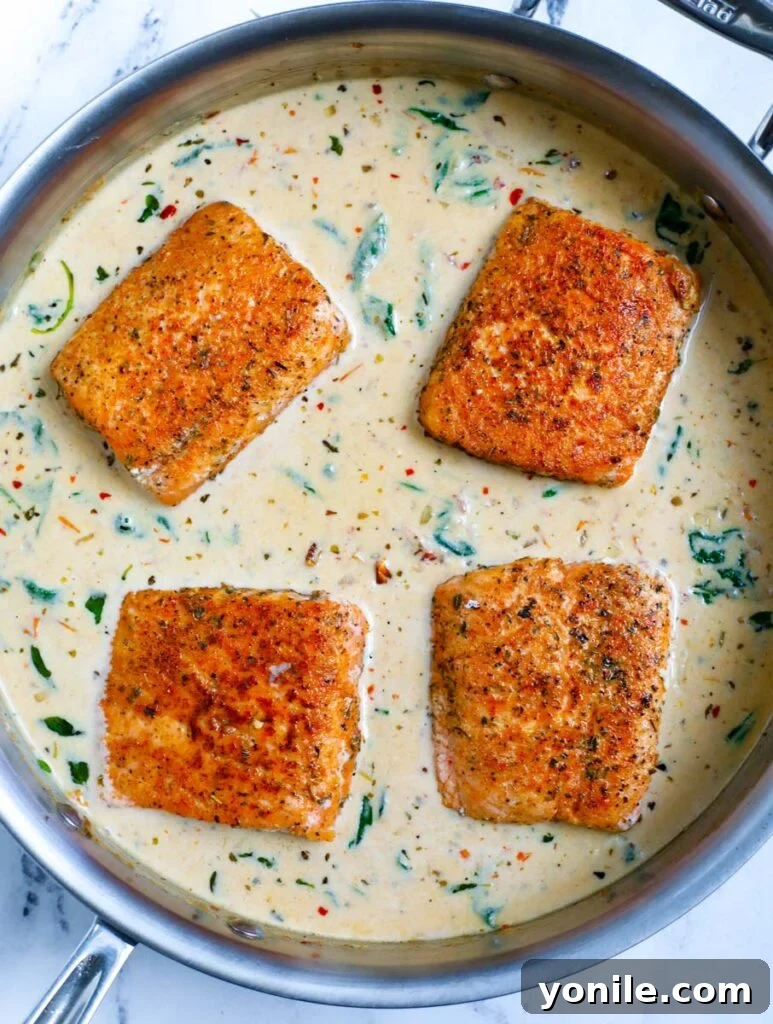 Overhead shot of salmon fillets simmering in cream sauce within a skillet.