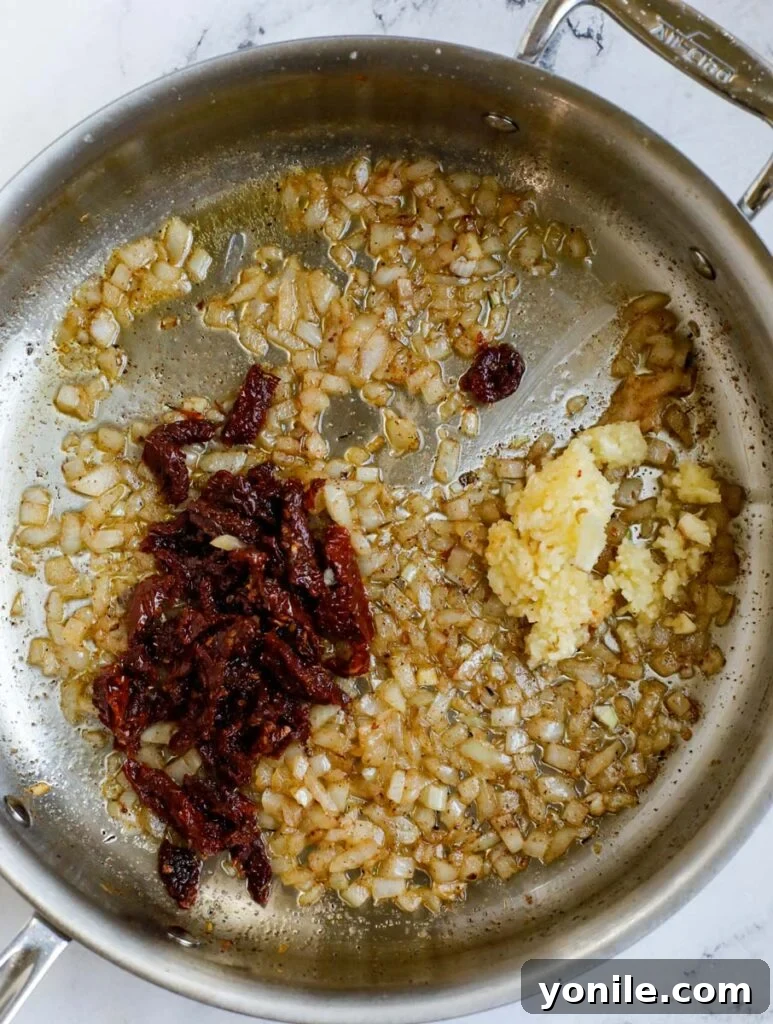 Top down view of sautéed onions, garlic, and sundried tomatoes in a skillet.
