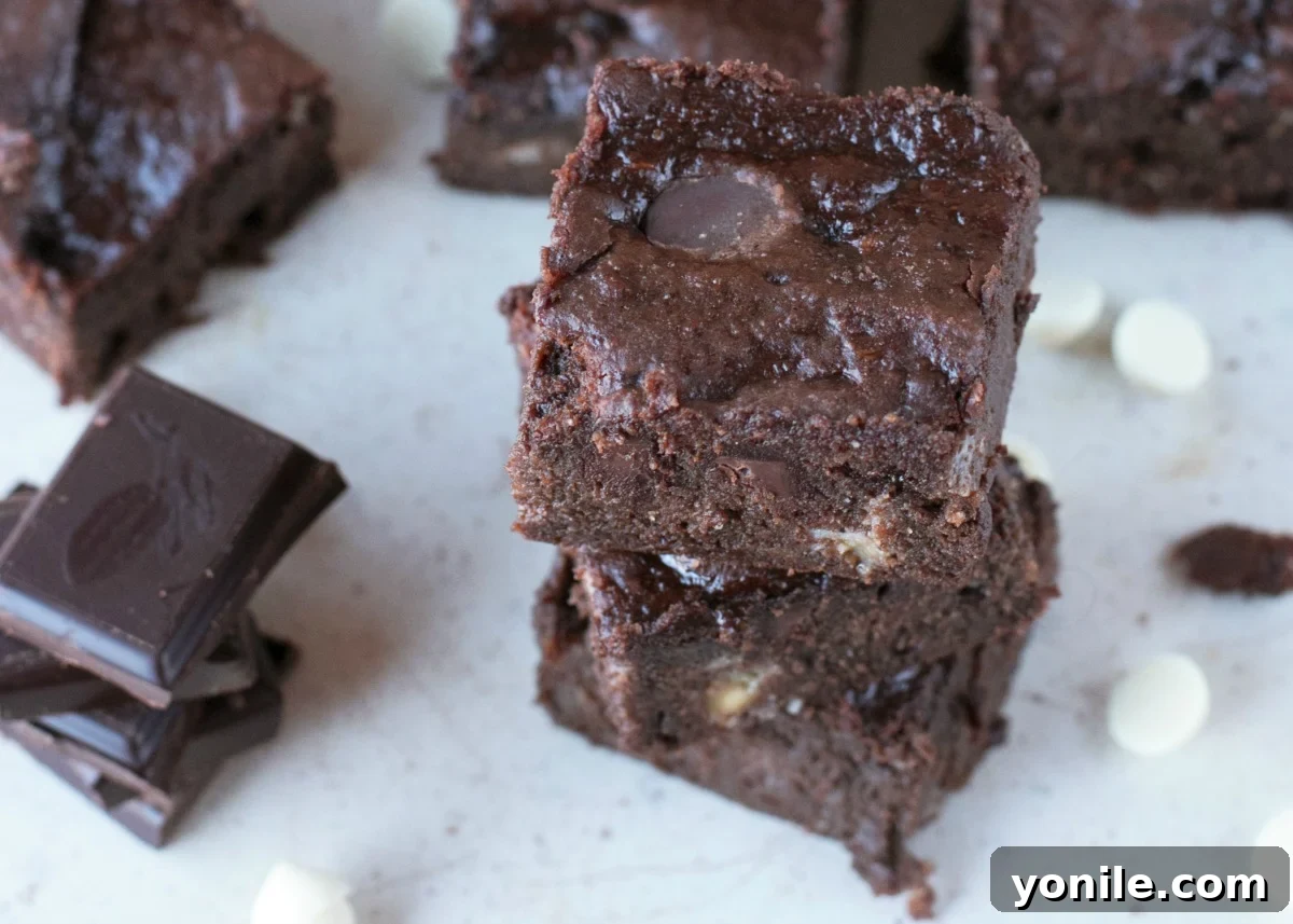 Stacks of cut triple chocolate brownies on parchment paper with chips and chunks of chocolate