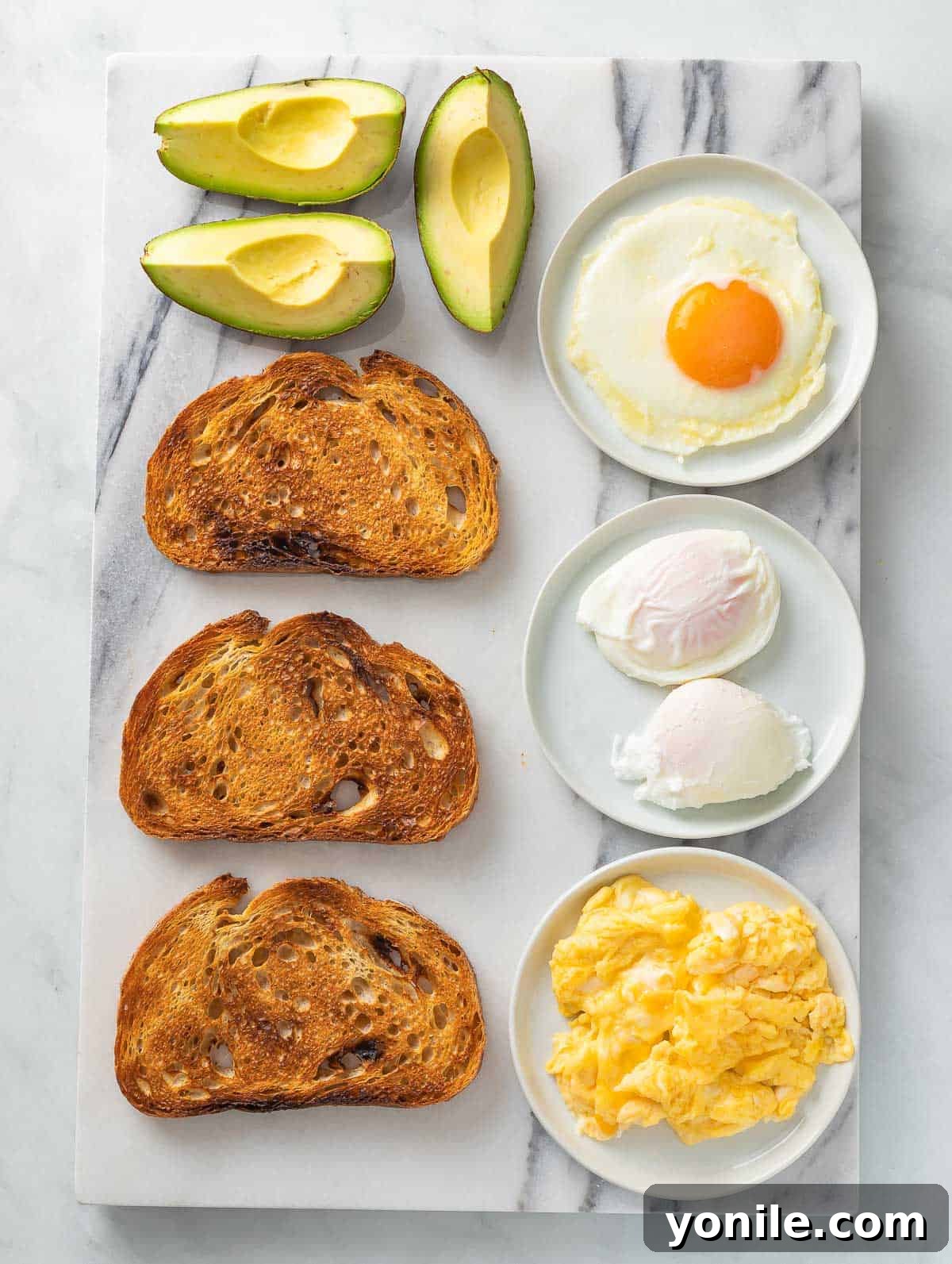 The Perfect Avocado and Egg Toast 3 Various ingredients for avocado toast laid out on a clean surface, including fresh avocados, a lemon, a pepper grinder, salt flakes, and red pepper flakes, alongside an egg.