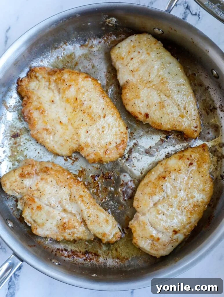 Top down view of golden-brown chicken breasts sizzling in a non-stick skillet.