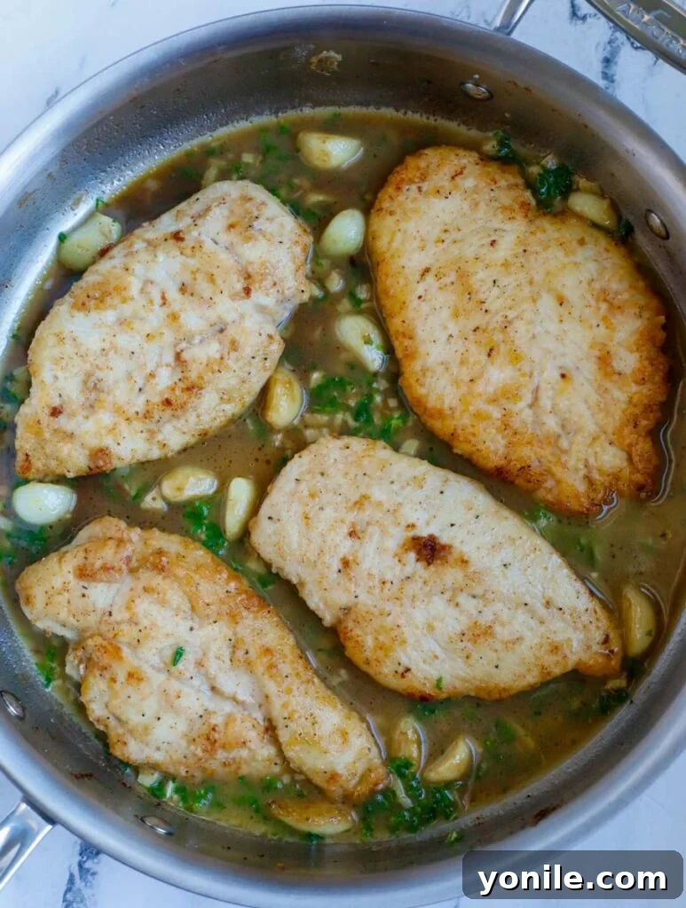 Top down view of the finished lemon garlic chicken in a skillet, perfectly coated in sauce and garnished with parsley and lemon.